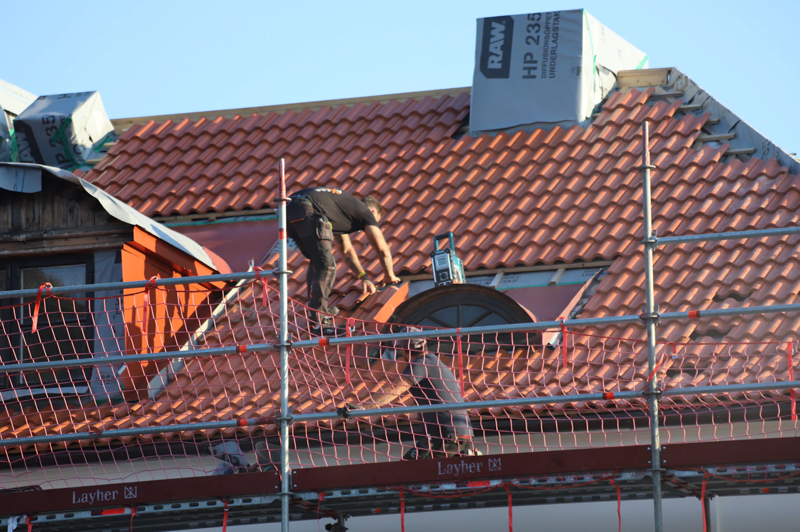 Dachdecker arbeitet auf einem roten Ziegeldach mit Gerüst